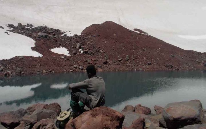 a teen sits near snow and water on backpacking trip 